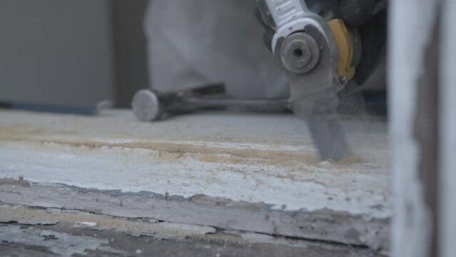 Man using an osillating tool to make a small groove in an old piece of wood.