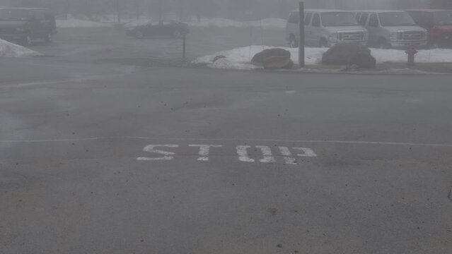 Parking lot during winter time in the fog with a stop sign painted on the road.