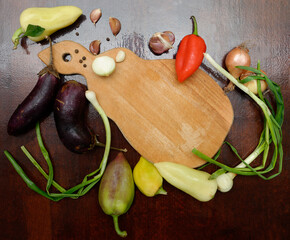 onion, garlic, sweet pepper, eggplant scattered on a dark wooden surface, around a cutting board,...