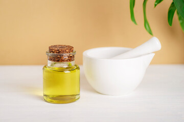 Natural cosmetic base oil and white ceramic mortar and pestle on white table on beige background. Natural cosmetics, skincare, and beauty product. Closeup