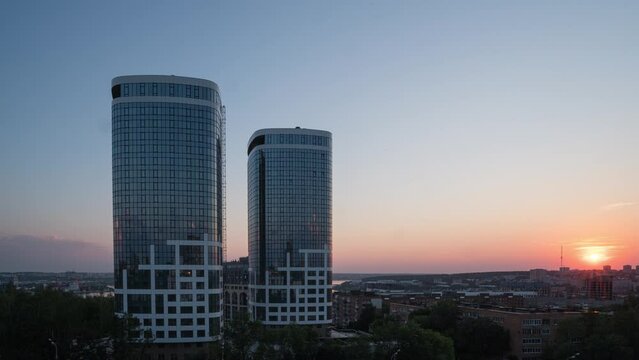 The Roofs Of Tall Concrete Skyscraper Towers In The Central Business District Of A Modern City Descend To Street And Ground Level With Small Local Houses. Sunset Time Lapse, Beautiful Cityscape.