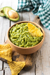 Mexican guacamole with nacho chip in wooden bowl on rustic wooden table. Traditional mexican food