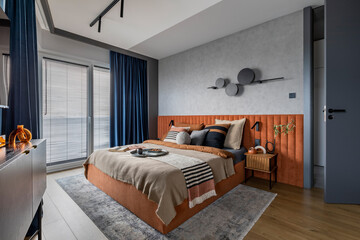 Interior design of elegant bedroom with big orange bed, beige and grey bedclothes, blue curtain,...