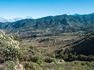 Dramatic lush green picturesque valley with old village Las Portelas. Landscape with sharp rock formation, hills and cliffs seen from mountain road, Tenerife, Canary Islands, Spain. sunny winter day