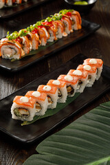 Sushi on black plate served with soy sauce, wasabi and ginger over grey background. Traditional Japanese food.