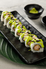 Sushi on black plate served with soy sauce, wasabi and ginger over grey background. Traditional Japanese food.
