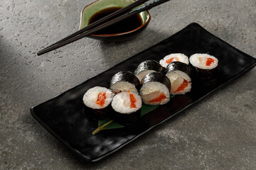 Sushi on black plate served with soy sauce, wasabi and ginger over grey background. Traditional Japanese food.