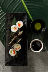 Top view of sushi on black plate served with soy sauce, wasabi and ginger. Traditional Japanese food.