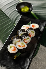 Sushi on black plate served with soy sauce, wasabi and ginger over grey background. Traditional Japanese food.