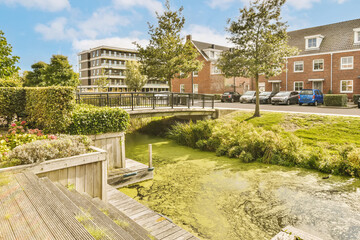 a river in the middle of a residential area with trees and flowers on either side of the water, there is a small bridge - obrazy, fototapety, plakaty