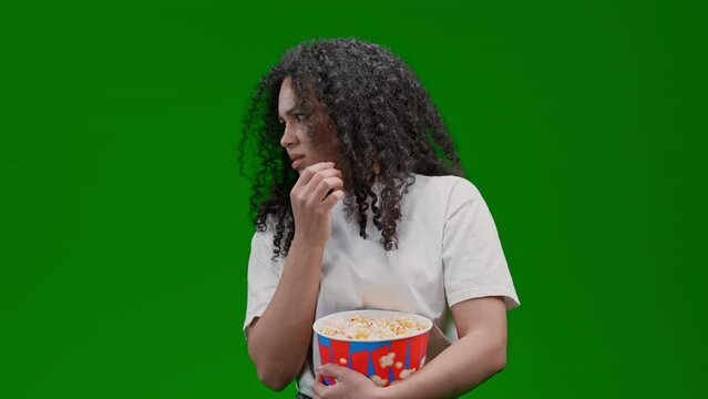 frightened woman with curly long hair dressed white tee eating popcorn watching horror Isolated on Green Screen