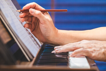 close up male musician hand writing a hit song while playing acoustic piano. songwriting concept