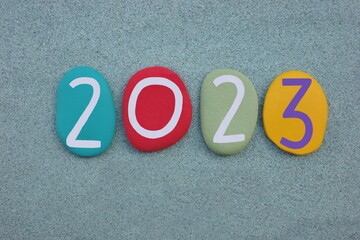 Year 2023 composed with hand painted multi colored stone numbers over green sand