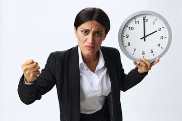 Business woman holding a wall clock in a black business suit and glasses showing signals gestures...