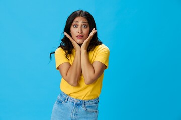 Woman in yellow t-shirt on blue background posing gestures emotions and signals with smile, hands up happiness copy space