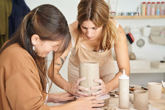 Two women working with clay in a pottery workshop. Craft, art and hobbies concept.