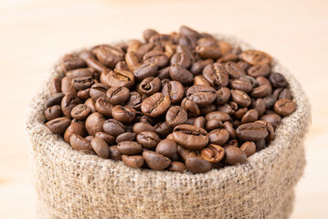 Coffee beans in linen sack against wooden background. Aromatic roasted coffee beans in a bag