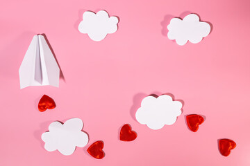A paper airplane on a red background among clouds and red hearts. Conceptual background for Valentine's Day or Women's Day. Copy space