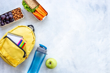 School lunchbox with fruits and yellow backpack, top view