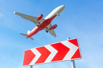 Airplane flying in the sky, landing over a sign with striped red and white arrows indicating the...