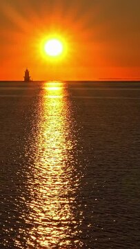 Beautiful sunrise with lighthouse at distance and sun reflection in ocean