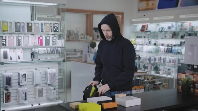 Suspicious man steals in a gadget store. The thief hides the goods and runs away from the store.