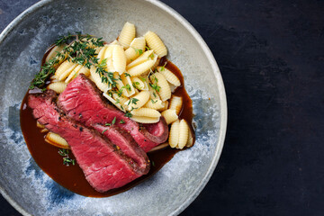 Traditional Italian chianina sliced roast beef with gnocchetti sardi pasta in spicy red wine sauce served as top view in a Nordic design bowl with copy space right