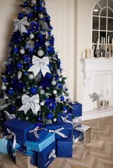 Decorated Christmas tree with blue toys and bows at home near the fireplace