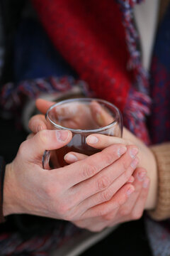 A couple in love warms themselves with hot tea in winter. Male and female hands. Love exists. Transparent cup