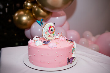 A sweet cake for a girl's birthday is decorated with pink cream and toys. A lot of sugar. Holiday mood