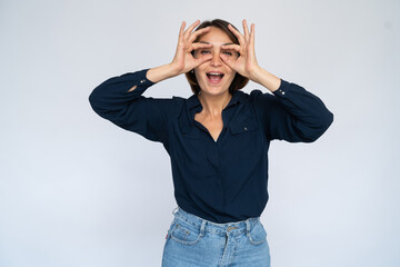 Funny woman making glasses with fingers. Female model in dark blue shirt putting fingers at face in shape of glasses. Portrait, studio shot, grimacing, fun concept