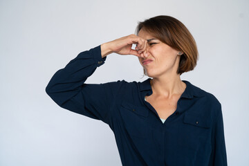 Disgusted woman covering nose. Female model in dark blue shirt smelling something bad. Portrait,...