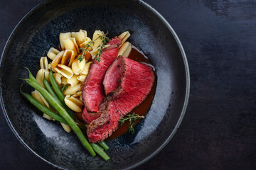 Traditional Italian chianina sliced roast beef with gnocchetti sardi pasta and beans in spicy red wine sauce served as top view in a Nordic design bowl with copy space right