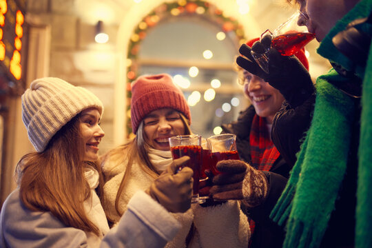 Group of young people, boys and girls spending time together at festive Christmas street, tasting hot mulled wine and coffee. Concept of winter holidays, emotions, friendship