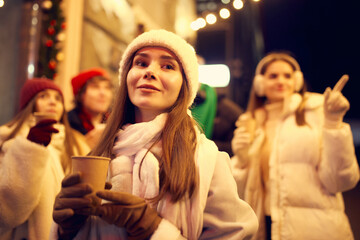 Happy beautiful young woman enjoying a cup of mulled wine on christmas market, street fair, outdoors. Holidays, emotions, hobbies, leisure activities