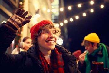 Emotional young people, friends meeting, smiling, drinking hot drinks at evening city street at winter time. Emotions, love, friendships, ad, sales concept