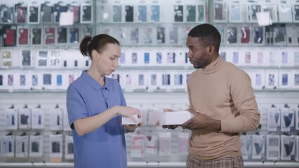 In a gadget and accessory store. Woman seller consultant, tells the man buyer about the goods.