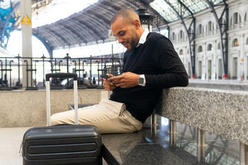 Smiling black businessman chatting on smartphone while sitting at train station