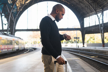 Black businessman checking time on wristwatch while standing on railway platform