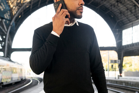 African American man talking on smartphone while standing on railway platform