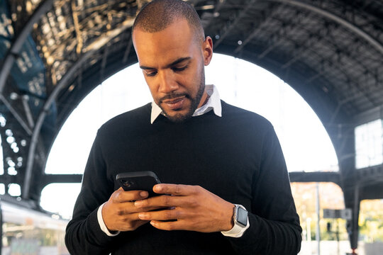 Smiling African American man on smartphone while standing on railway platform