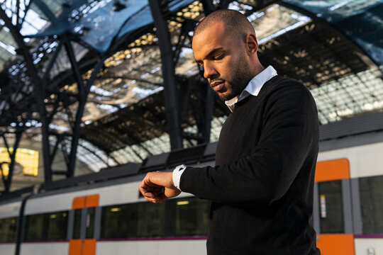 Black businessman checking time on wristwatch while standing on railway platform