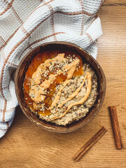 Oat porridge with persimmon, cinnamon and peanut butter in a coconut bowl.