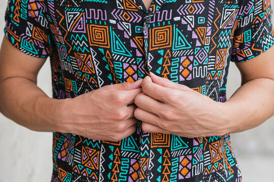 Crop man buttoning up colorful shirt