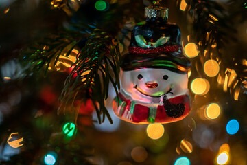 Schneemann Christbaumschmuck an einem Weihnachtsbaum. Im Hintergrund ein Bokeh bunter Lichter.