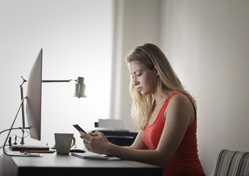 portrait of young woman sitting at table while working with computer and smartphone