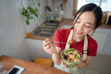 Portrait of a young and cheerful woman eating healthy salad in the kitchen at home. Healthy eating, wellbeing, and lifestyle concept