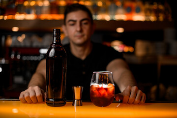 Close-up front view on jigger and bottle and glass with iced drink on bar counter