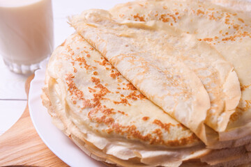 Stack of thin pancakes on plate and glass of milk
