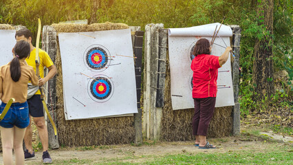 Back view of female officer wear face mask collect arrows fired from a bow on sport target. Woman...